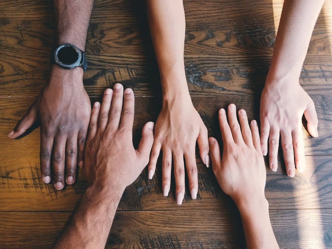 Four people's hands resting side by side on a wooden table