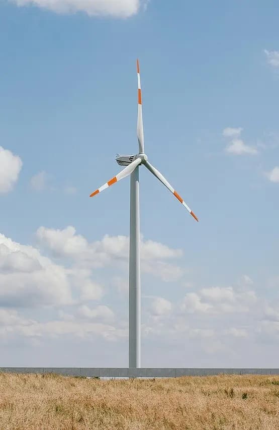 A single wind turbine standing in an open field under a partly cloudy sky