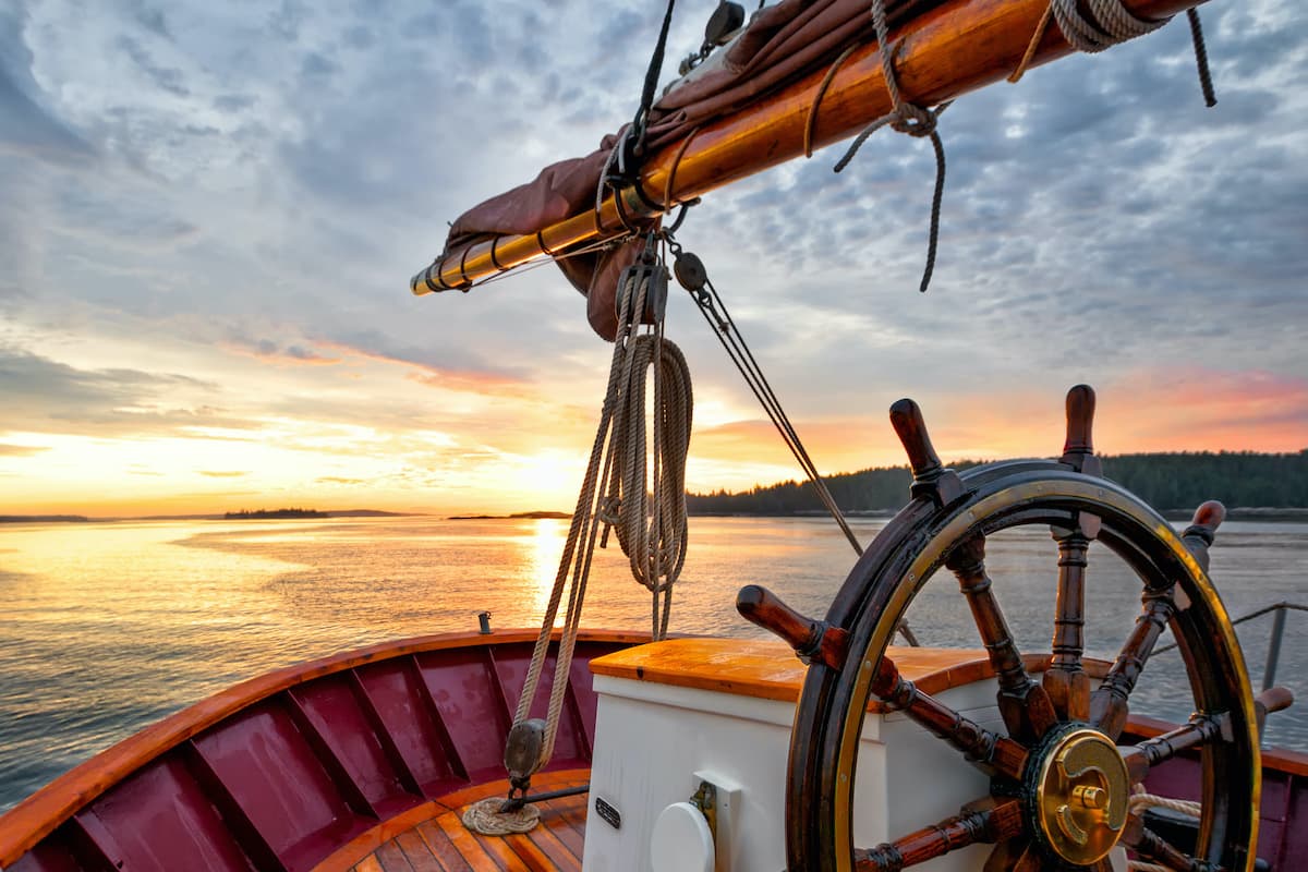 A ship's wheel at sunset as the vessel navigates toward the horizon